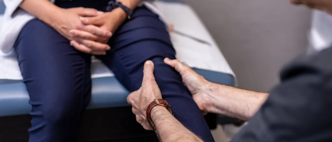Doctor examining patient's knee in medical office during a consultation for leg pain or injury.