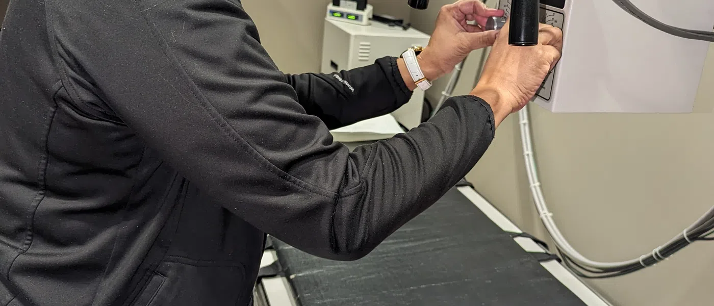 A medical technician operates an X-ray machine while a patient prepares for imaging.