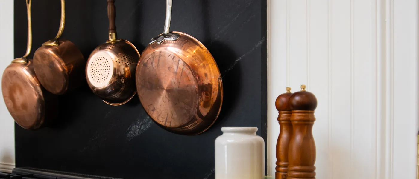 Copper pans hanging on black backsplash above stove with white ceramic jars and wooden salt and pepper grinders on counter.