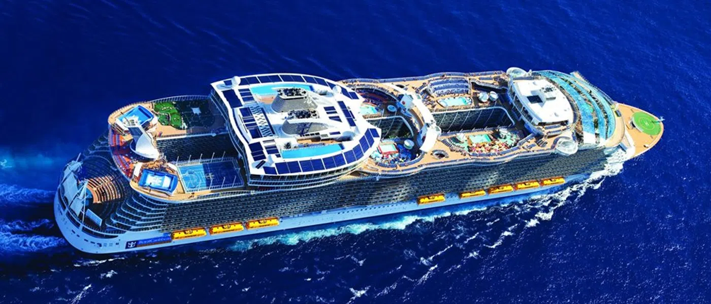 A large cruise ship sails through deep blue ocean waters with pools and recreational areas on deck.