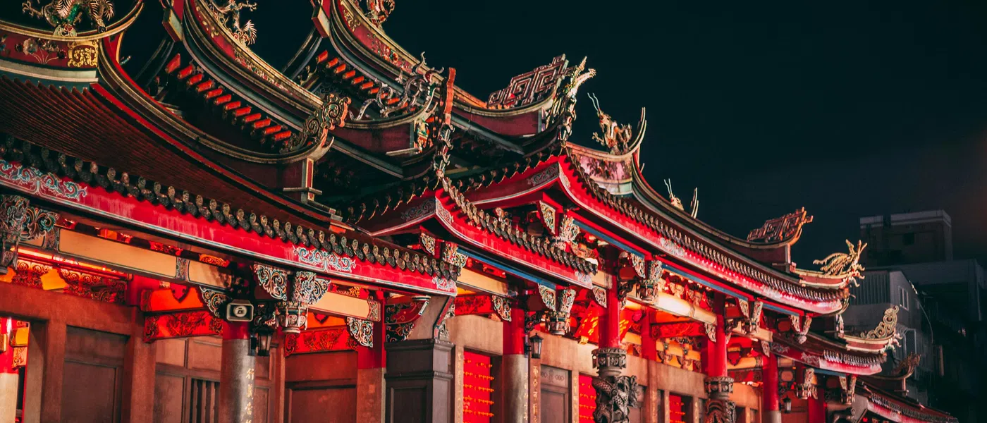 Traditional Chinese temple illuminated at night showcasing detailed red and gold ornate roof and carved pillars.