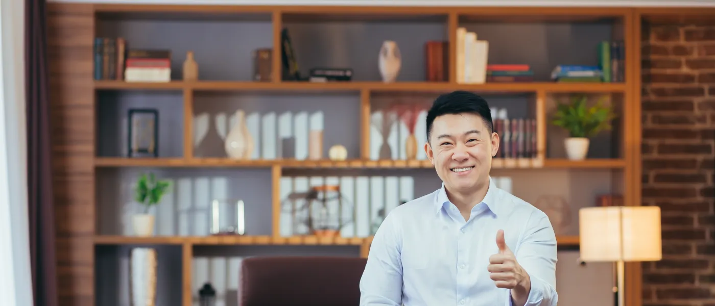 Smiling businessman giving thumbs up in modern office with bookshelf and desk globe in the background