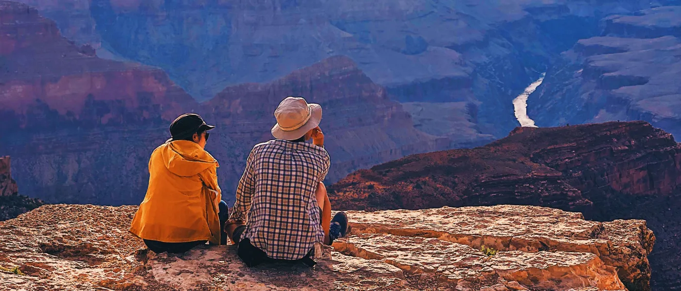 a couple of people sitting on a rock looking at a canyon