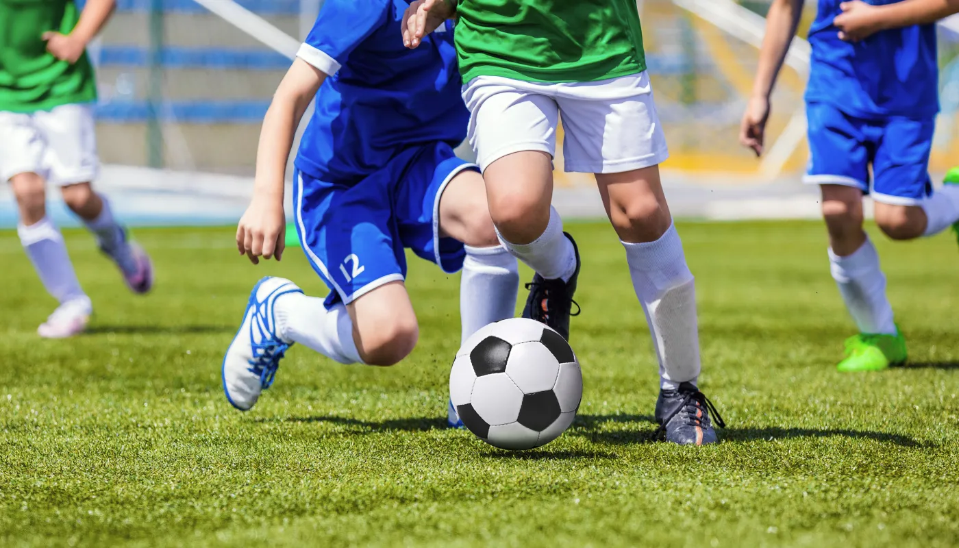 Youth soccer players in blue and green uniforms competing for the black and white ball on a grassy field.
