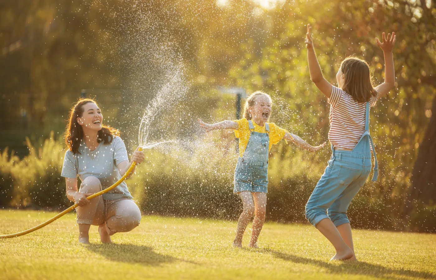 Mother and two kids playing and laughing with garden hose in Greer, SC