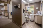 Modern dental office with dental chair, computer monitor, and medical equipment near window with blinds.