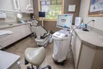Modern dental office with dental chair, imaging machine, computer screen showing dental scan, and window with blinds.