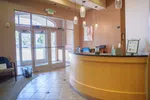 Modern reception area with curved wooden desk, hanging lights, and glass entry doors in a welcoming office lobby.