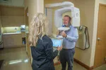 Man undergoing dental 3D X-ray scan operated by technician holding control tablet in clinic room