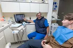 Dentist explains dental X-ray results to a seated male patient in a modern dental office.