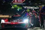 Acura race car in pit stop with crew refueling and changing tires during night race event.