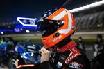 Race car driver in American flag helmet preparing at night pit stop with race cars and illuminated lanes in background