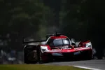 Red Acura race car with bright LED headlights racing on a dark track surrounded by trees.