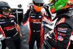 Race car driver adjusting helmet while team members in matching DEX Imaging suits prepare in garage pit area
