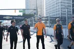 Group of race team members walking on city street near Chevrolet racing banners under bright sunlight.