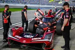 Pit crew performs maintenance on red Acura race car during motorsport event with officials overseeing.