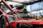 Red Acura prototype race car with open door in a well-lit garage or pit area.