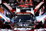 Front view of Acura race car with raised doors and team crew blurred in background.