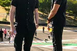 Two men in black Acura DEX racing team shirts standing on a racetrack on a sunny day holding drinks.
