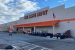 The Home Depot storefront with an outdoor display of grills, chairs, and gardening supplies under a partly cloudy sky.