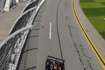 Red and black race car speeding on a curved asphalt track with empty grandstands at a professional racing circuit.