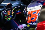 Race car driver wearing a colorful helmet inside a high-tech cockpit with illuminated steering wheel controls.