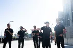 Group of seven men in black uniforms standing and talking outdoors on a sunny day casting long shadows.