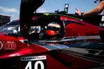 Race car driver in red and black Acura prototype car number 40 during pit stop with crew member wearing headset.