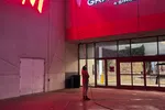 Person in red jacket holding a long pole under glowing H&M and Grapevine Mills mall signs at night.