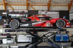 Red and black race car number 40 elevated on a hydraulic lift inside a garage with tools and equipment.