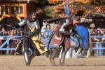 Two medieval knights in armor engaged in a staged sword fight during a fall festival with autumn trees in the background