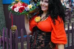 Smiling woman in Renaissance attire holding a flower basket and a yellow rose at a festival.