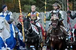 Four medieval knights in armor on decorated horses holding lances during a jousting event outdoors.