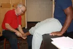 Doctor examining patient's ankle in a medical office with stethoscope and paperwork on the desk
