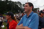 Coaches and staff smiling on the sidelines during a football game with players and spectators in background