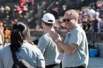 Smiling man in sunglasses clapping among casually dressed people at outdoor event with crowd in background
