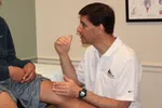 Doctor examining patient's knee and discussing treatment in a medical office setting.