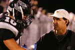 Football player in black helmet listens to coach wearing white cap during nighttime game.