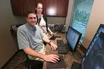 Man and woman working together at office desk with computer monitors and window view of street outside