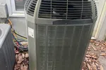 AC Repair in Peachtree Corners by The Air Company of GA.  Outdoor air conditioning unit with tool bags on top and dry leaves scattered around on the ground.