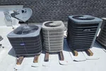 Smyrna HVAC Diagnostic Repair and Replacement by The Air Company of GA.  Three rooftop air conditioning units on wooden blocks with a satellite dish and shingled roof background under a sunny sky.