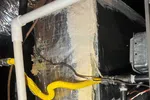Heating Furnace Repair in Alpharetta 30009 by The Air Company of GA.  Close-up of HVAC system ductwork with insulation, wiring, and a yellow flexible gas line in a basement ceiling.