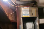 AC Heating Repair on Furnace in Atlanta 30327 by The Air Company of GA.  Open HVAC unit installed in attic with exposed ducts, pipes, and wiring under a bare bulb light.