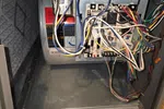 Open HVAC system showing wiring, circuit board, and fan assembly inside a metal casing with multi-colored wires.