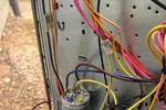 Residential Heating Furnace HVAC Repair in Dunwoody 30338 by The Air Company of GA.  Close-up of colorful electrical wires connected to a metal panel with a capacitor and relay outdoors.