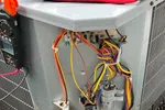 AC Repair in Roswell 30076 by The Air Company of GA. Outdoor HVAC unit with open panel showing internal wires, capacitor, and electrical connections on mulch ground.