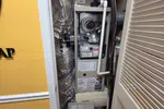 Commercial AC Heating Repair in Atlanta Dunwoody 30338 by The Air Company of GA.  Opened furnace unit in a closet with exposed pipes, ducts wrapped in foil insulation, and a tool bag on wooden floor.