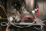Interior view of a furnace showing metal ductwork, wiring, gas valve, fan, and electrical components inside the unit.