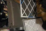 Two HVAC air filters next to an open furnace with tools on a wooden floor during maintenance.