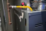 Commercial HVAC Repair in Dunwoody 30338 by The Air Company of GA.  Close-up of a gas furnace with yellow flexible gas line connected to metal pipe inside a utility room.